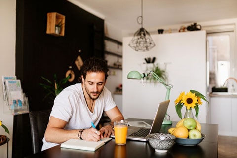 A man seated at a desk at home and writing in a ledger.